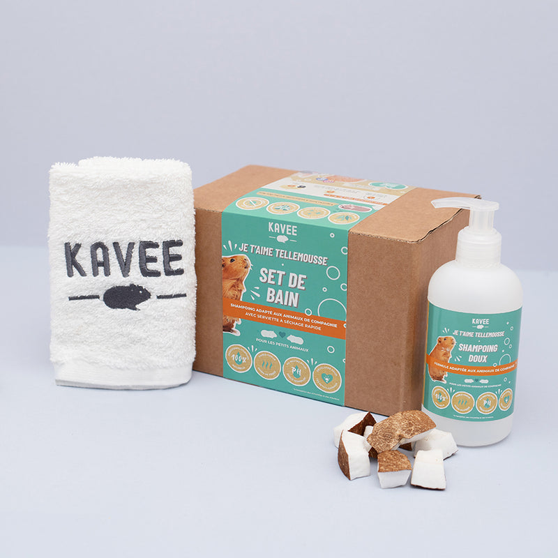 Set de bain de la marque Kavee avec des morceaux de noix de coco, le shampoing et la serviette de bain à coté sur fond gris